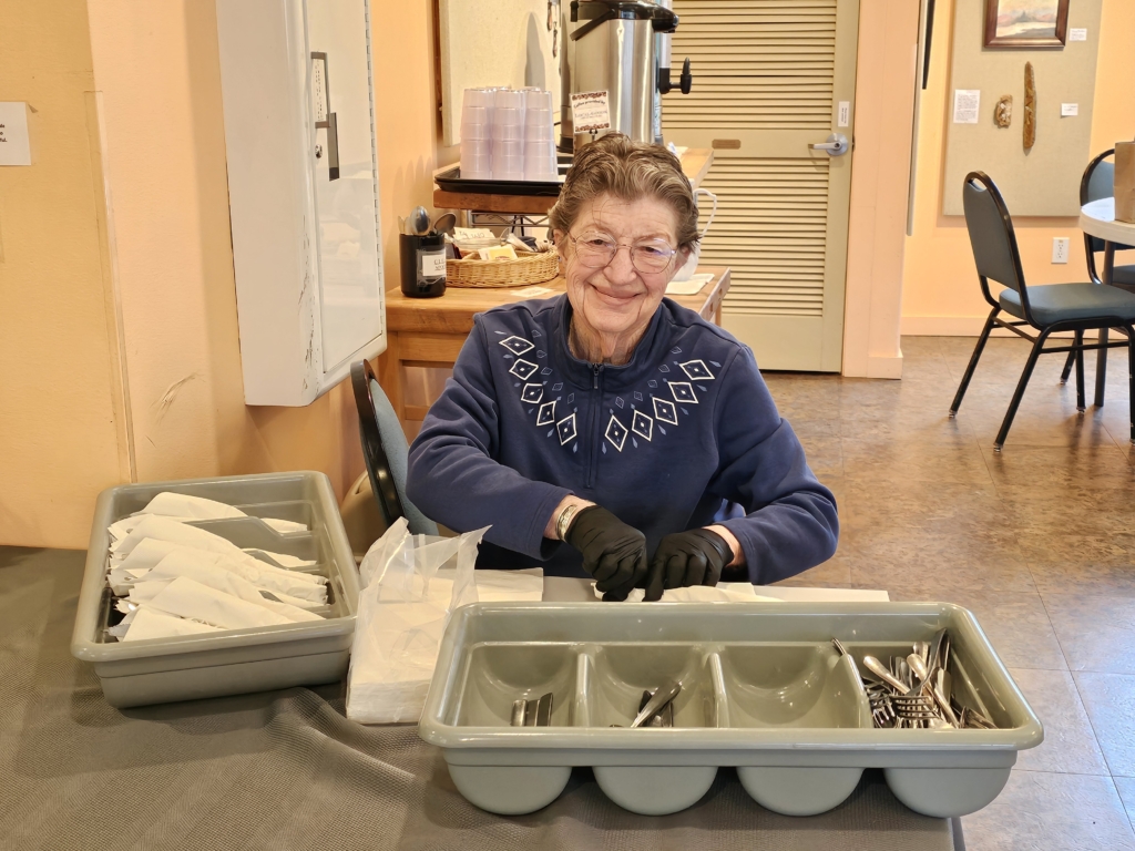Volunteer wrapping silverware in napkins for Senior Lunch